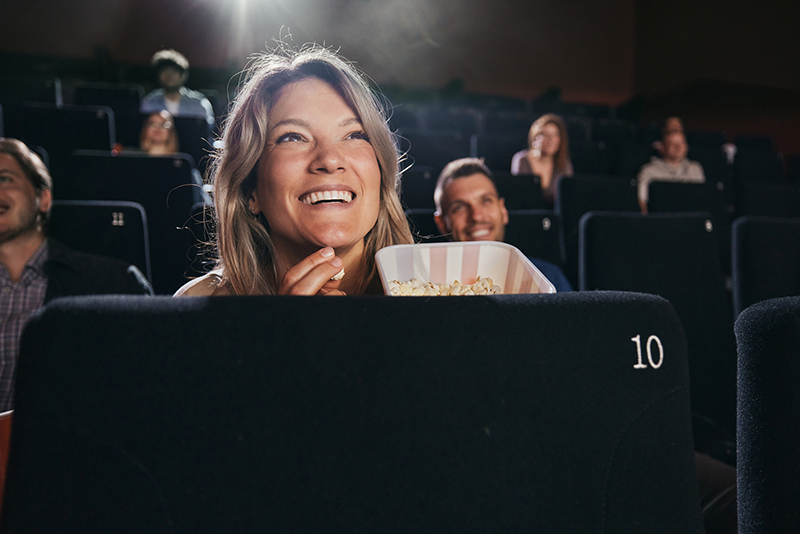 Happy woman eating popcorn while watching a movie in cinema.